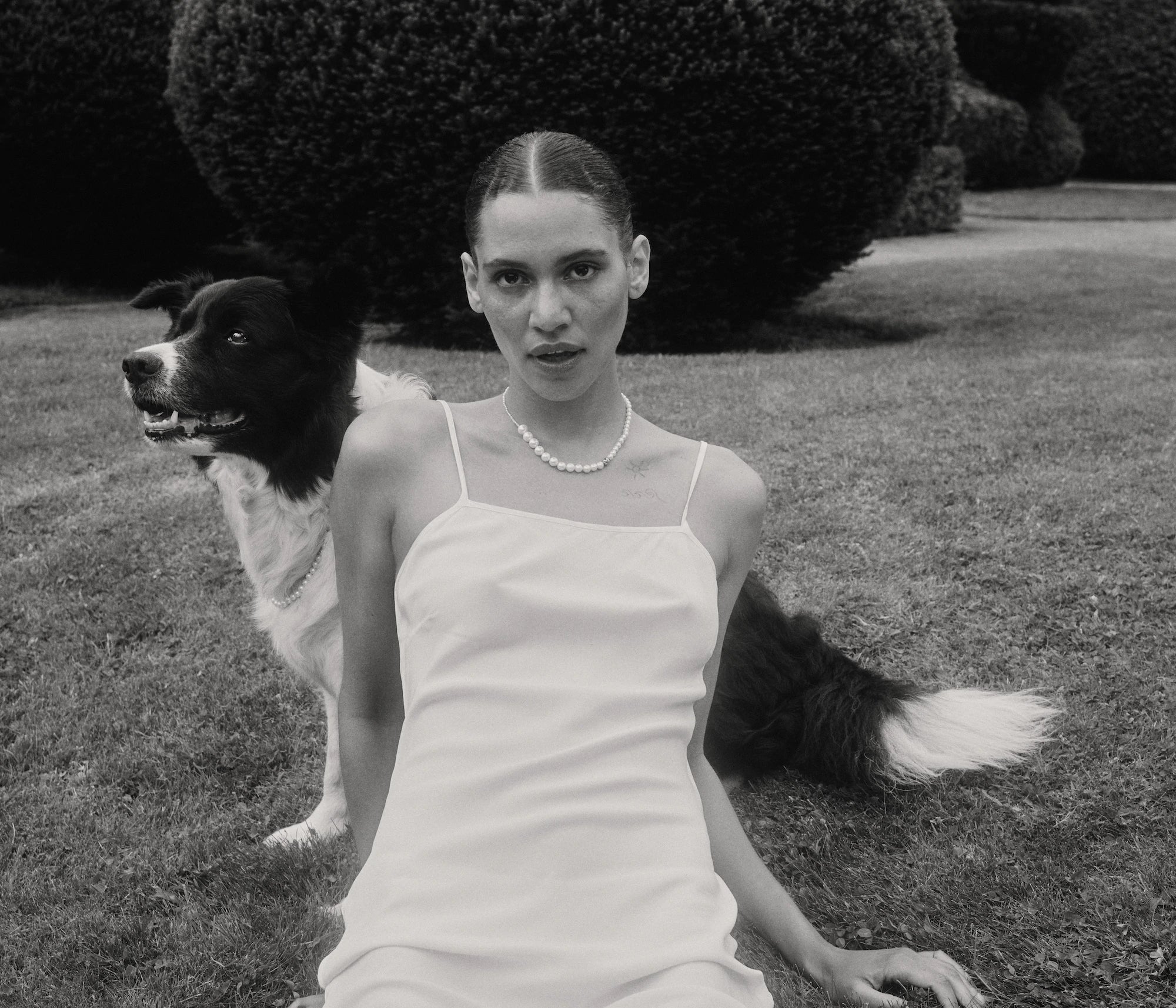 Black and white photography of model wearing Peggy pearl necklace while laying on the grass