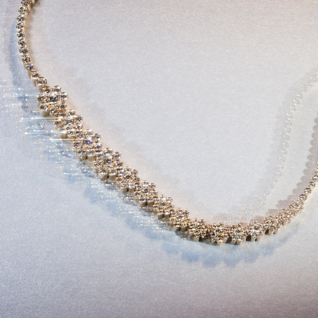 The Fleur de Tennis diamond necklace with graduating diamonds in a flower motif displayed as a still life image on a light grey background.