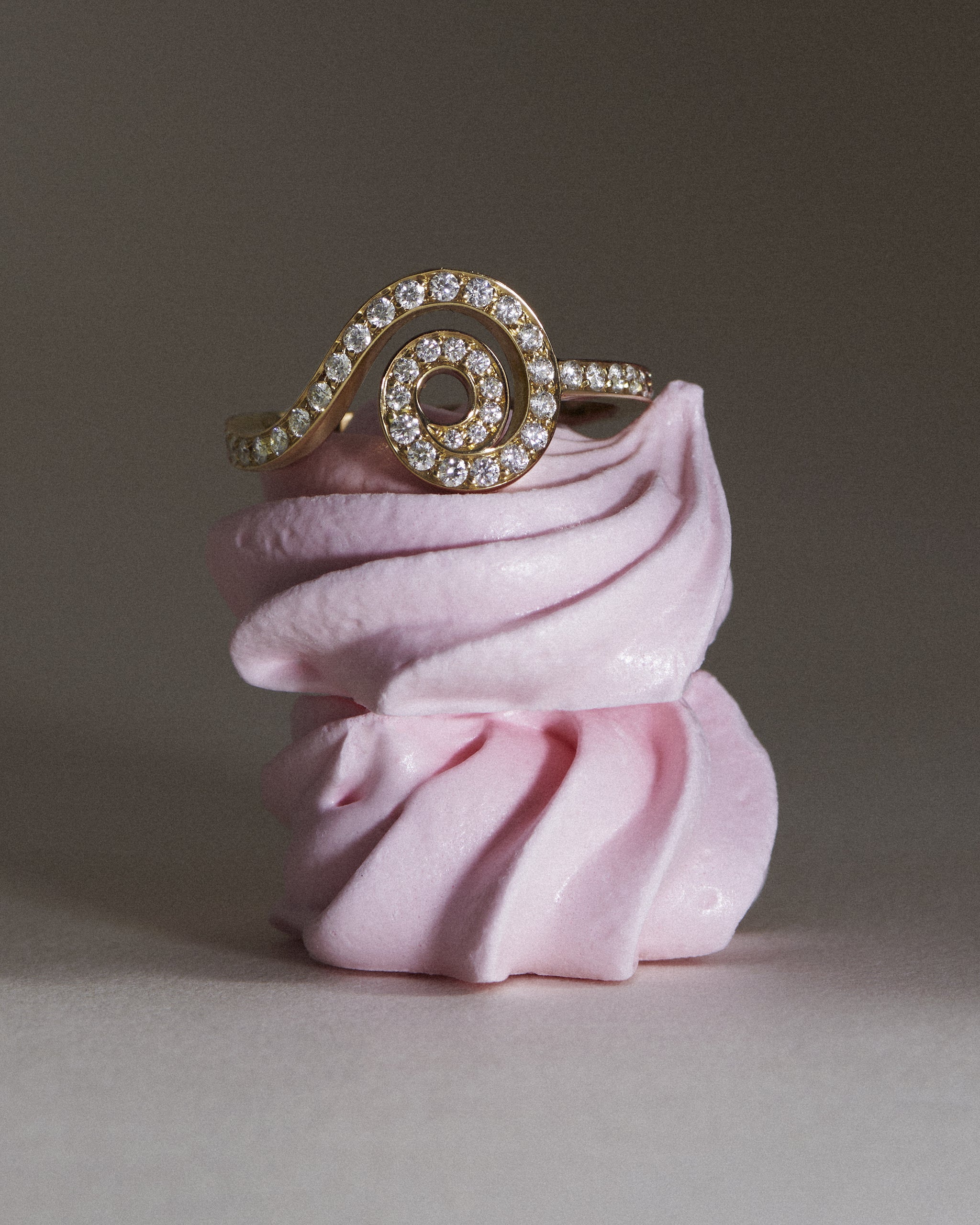 The La Dorset Pavé 18K yellow gold diamond ring is placed on top of two stacked rose meringue 'kiss' candy cakes.