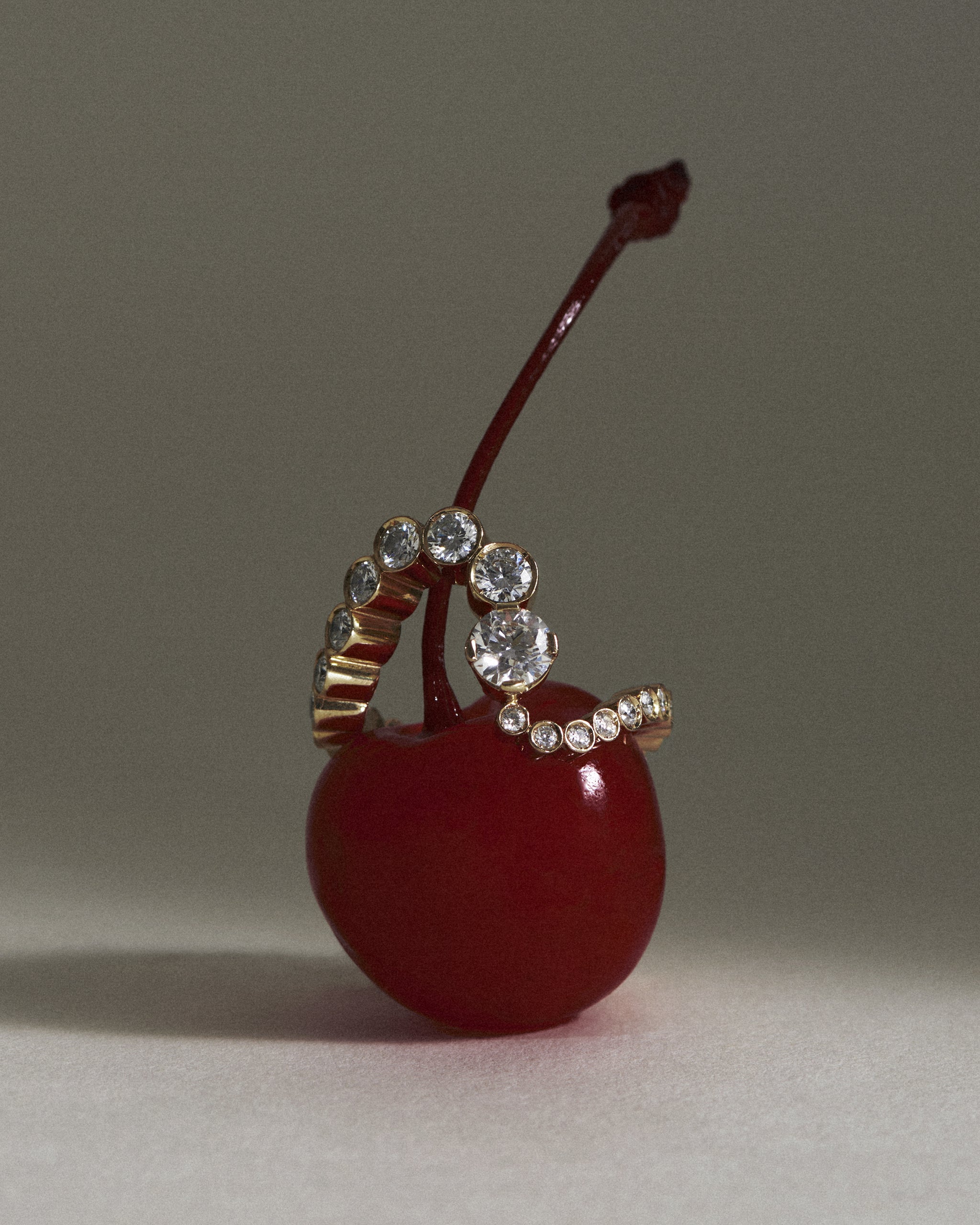 The Grand Ensemble Ocean 18K yellow gold diamond ring is placed on top of a red cherry.