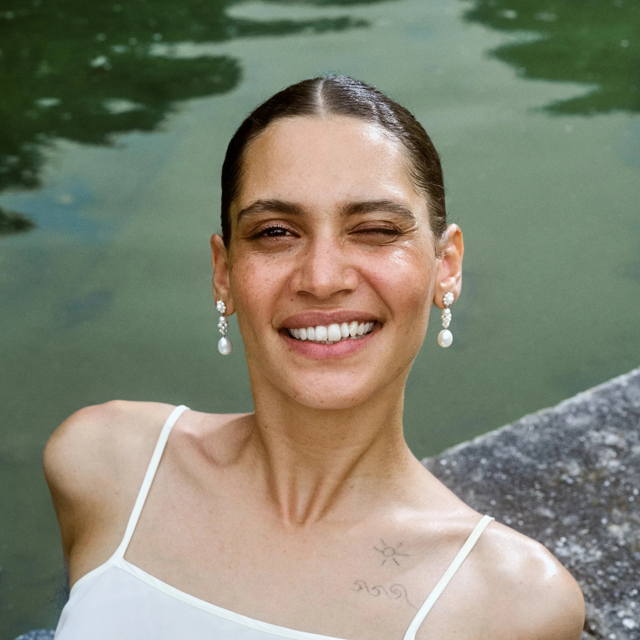 Model laying next to a pool, wearing Bellis L'Eau pearl earrings