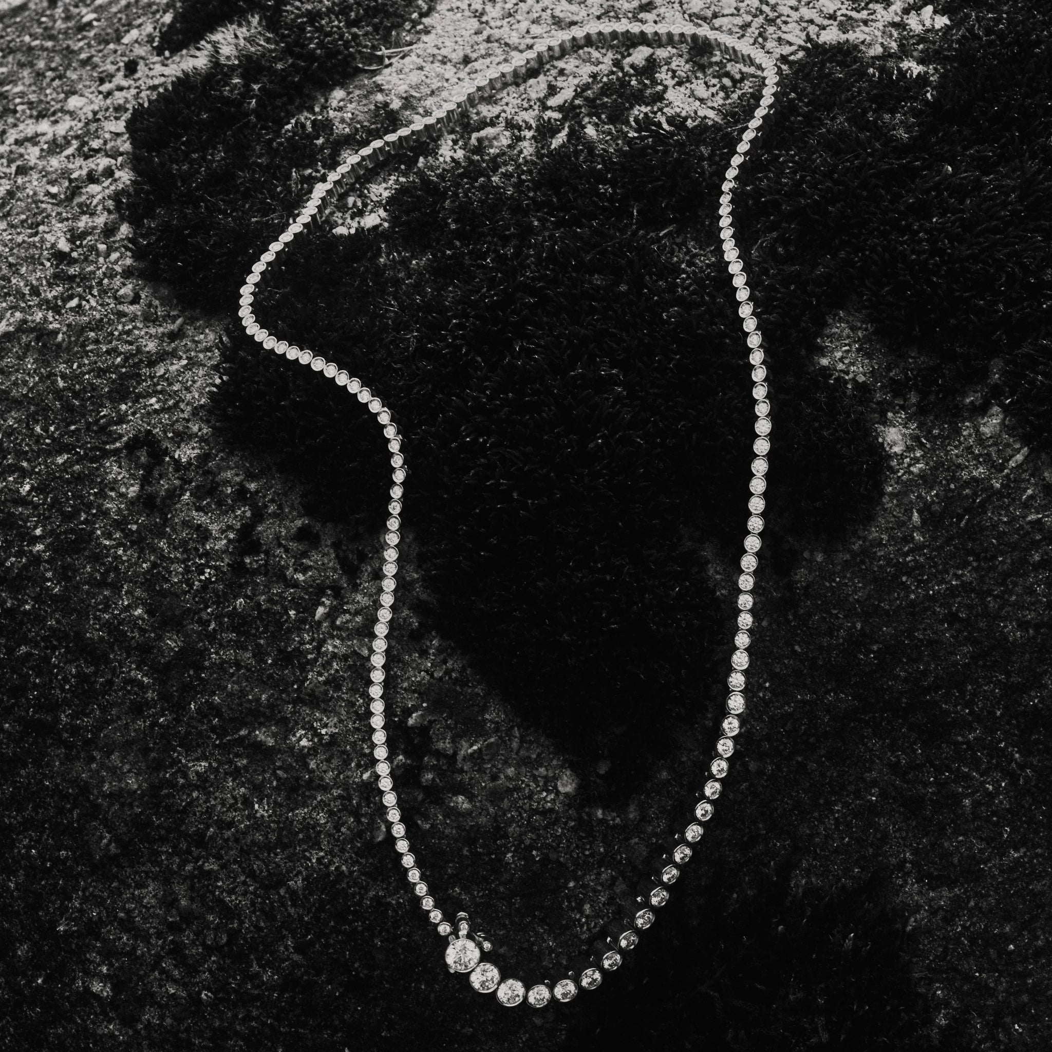 Black and white photography of Collier de Tennis diamond necklace placed on a rock 